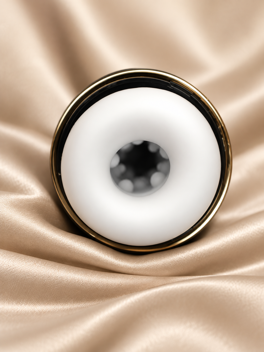 A close-up studio shot of a white circular ring-shaped product with a gold-toned rim, placed on draped champagne satin fabric.