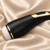 A sleek black handheld personal massager with gold trim and a white head, resting on draped champagne satin fabric.
