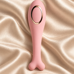 A pink silicone personal massager with a bone-shaped handle and a gold metallic oval accent, displayed on a draped champagne satin fabric background.