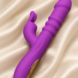 A purple dual-stimulation personal massager with a gold accent button, resting on a draped beige satin fabric background.