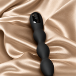 A matte black silicone wavy vibrator with a rectangular control panel on the end, resting on draped champagne satin fabric.