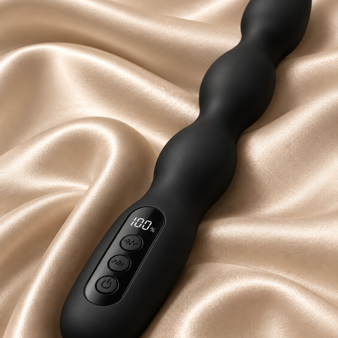 A black silicone wavy vibrator with an integrated digital display and control buttons, resting on draped champagne-colored satin fabric.