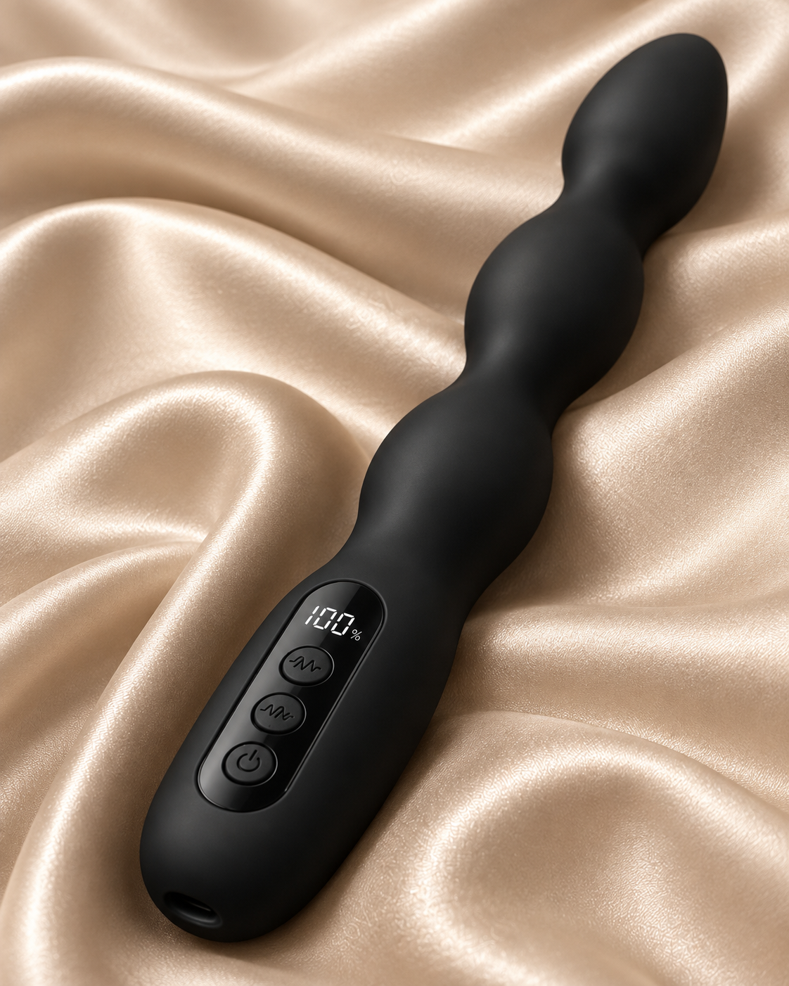 A black silicone wavy vibrator with an integrated digital display and control buttons, resting on draped champagne-colored satin fabric.