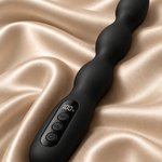 A black silicone wavy vibrator with an integrated digital display and control buttons, resting on draped champagne-colored satin fabric.