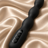 A black silicone wavy vibrator with an integrated digital display and control buttons, resting on draped champagne-colored satin fabric.