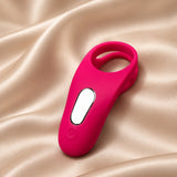 A bright pink personal massager with a sleek ergonomic design, a central white oval button, and a ring-shaped head, resting on a draped beige satin fabric background.