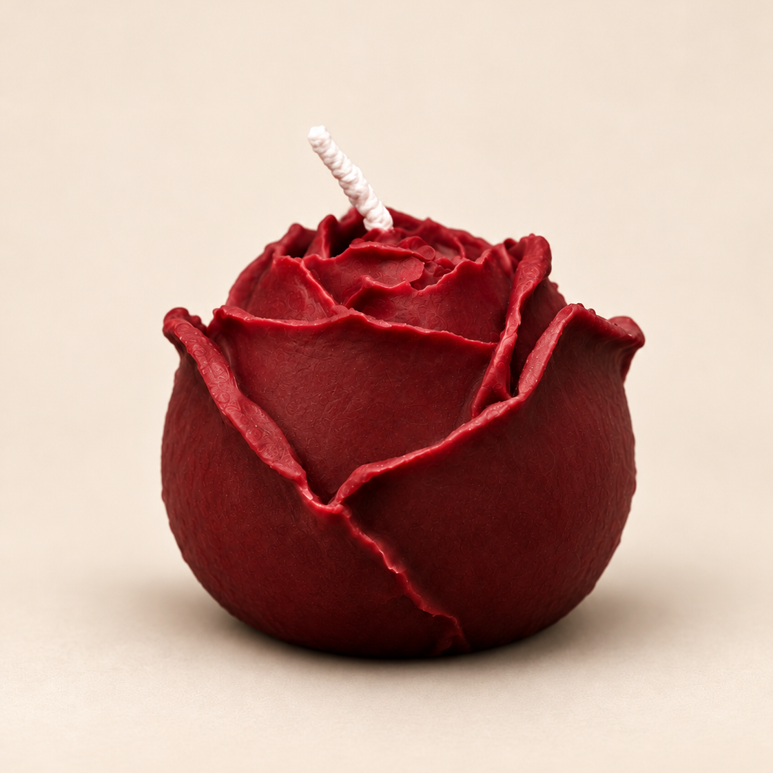 The Rose soy candle in burgundy on a warm beige background.