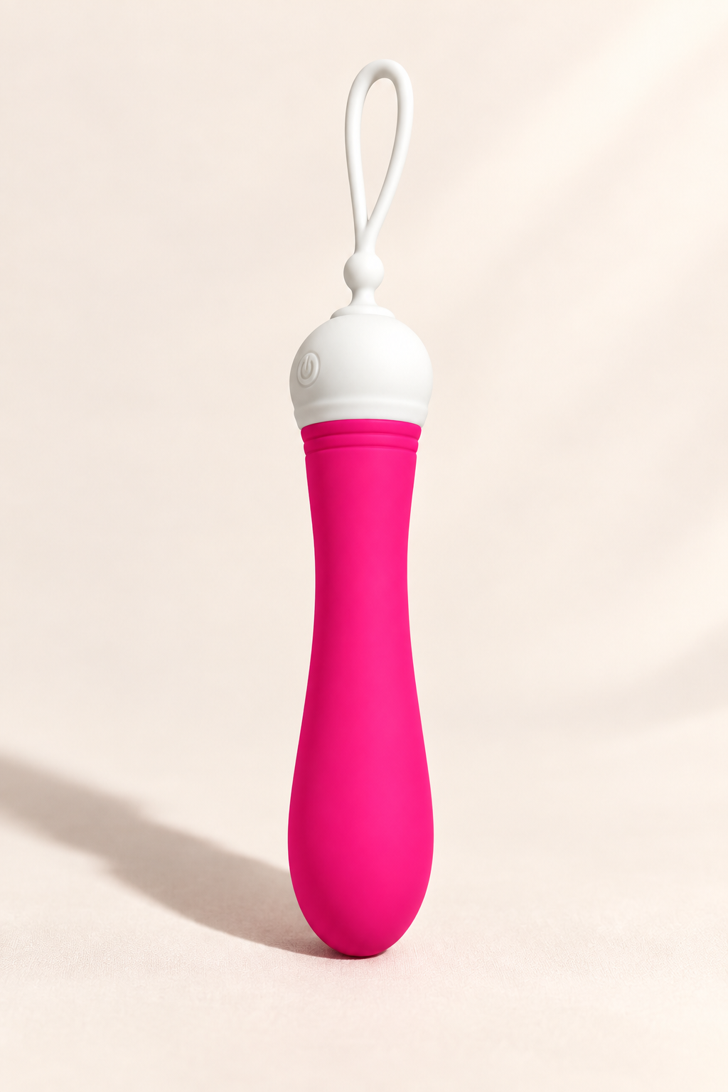 A pink and white personal massager with a curved silicone body and a white loop handle, standing upright on a light beige background.